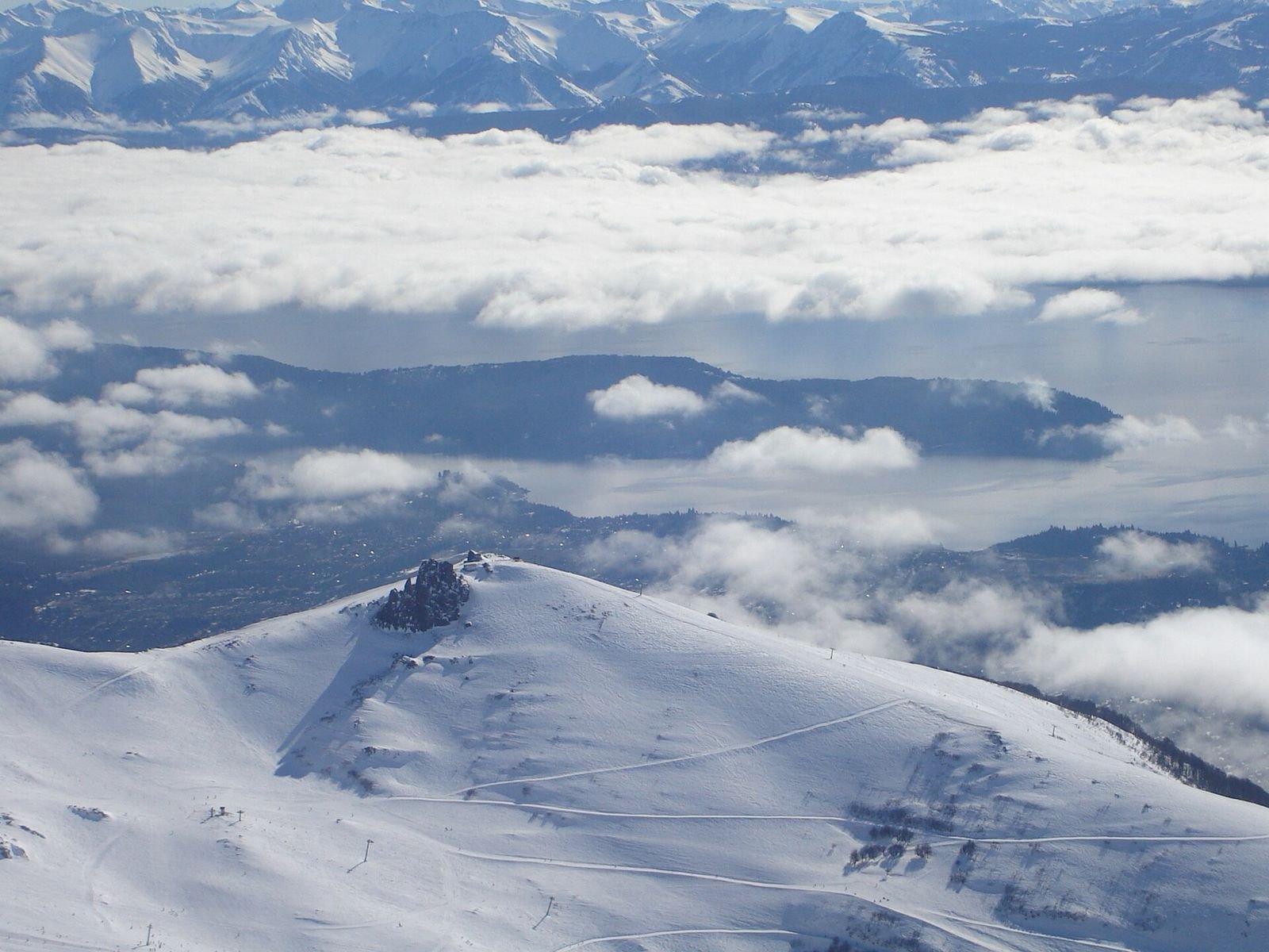 Pistas nevadas do Cerro Catedral acima das nuvens, com a Península San Pedro ao fundo